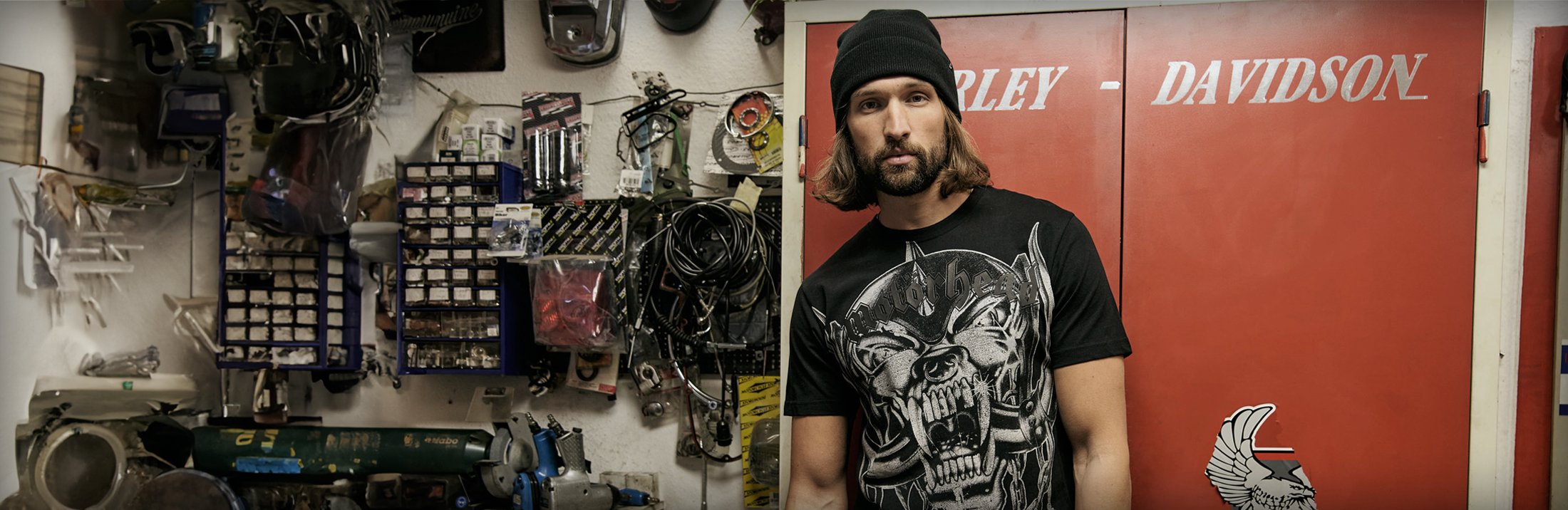 mies nojaa autotallin seinään päällään musta pipo ja musta t-paita