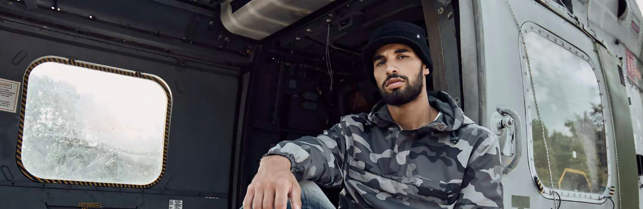 Mies mustassa hatussa ja camokuosisessa takissa istuu autossa