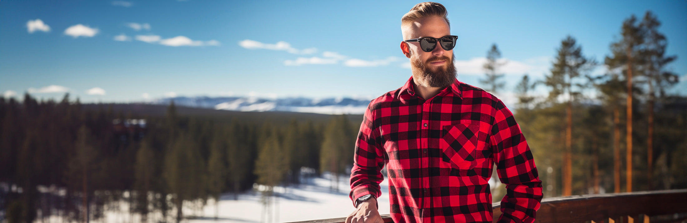 Hymyilevä mies seisoo terassilla auringon paisteessa, pukeutuneena mustapunaiseen ruutupaitaan ja mustiin aurinkolaseihin
