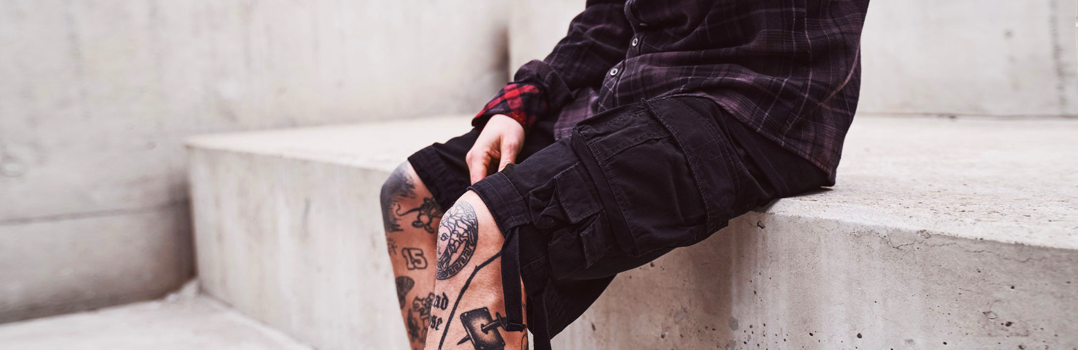 tatuoitu mies mustissa reisitaskushortseissa ja ruutupaidassa